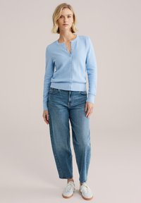 Svetlomodro teksturirano jopico z okrolim izrezom in gumbi, kombinirano z ohlapnimi jeans hlačami in belimi supergami.