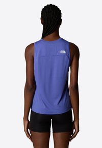 Top deportivo sin mangas de color púrpura con un escote redondo y un detalle de logo en la parte trasera; combinado con pantalones cortos de compresión negros. Tejido suave.