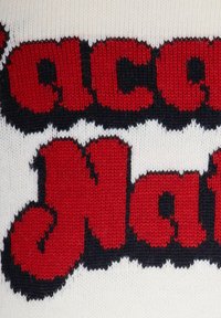 Maglione lavorato a maglia con testi rossi audaci su uno sfondo crema, con accenti blu scuro attorno alle lettere, che mostra un motivo di punto strutturato.