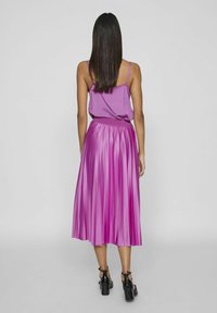 Top senza maniche viola e gonna midi plissettata, entrambe di un vivace rosa. La gonna presenta una texture liscia e una vita aderente. Scarpe con tacco nere.