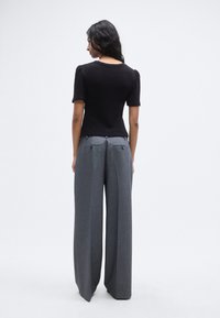 Μαύρο πλεκτό τοπ με κοντά φουσκωτά μανίκια, σε συνδυασμό με ψηλόμεσα γκρι φαρδιά παντελόνια με τσέπες στο πίσω μέρος και φερμουάρ ως διακοσμητικά στοιχεία.