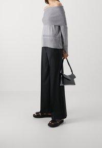 Top grigio off-shoulder in maglia con texture a coste, abbinato a pantaloni larghi neri e borsa nera. Le sandali presentano un design con cinghie intrecciate.