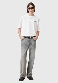 White cotton t-shirt with "ALLSAINTS" logo, paired with faded grey jeans and black belt. Black sunglasses and chunky black shoes complete the look.