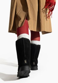 Botas de ante negras hasta la rodilla con un acabado texturizado y suelas de goma, con un detalle del logo dorado en la parte posterior.