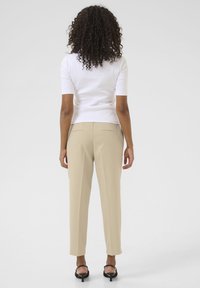Haut blanc à manches courtes associé à un pantalon beige bien coupé. Texture lisse, coupe slim et poches arrière discrètes ; des sandales à talons noirs viennent compléter le look.