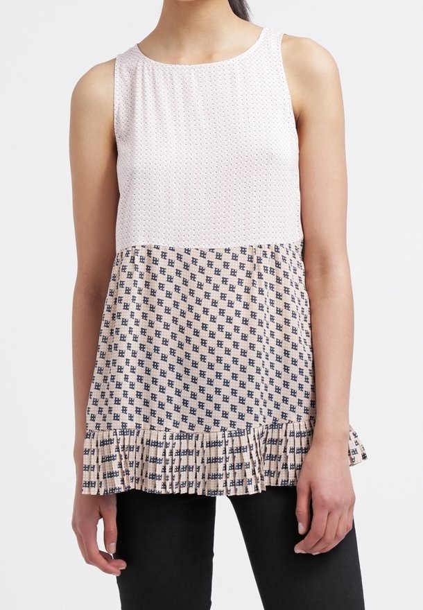 Ärmlös topp med en texturerad vit övre sektion och en mönstrad marinblå nedre sektion. Har en volangnederdel och en rund halsringning.