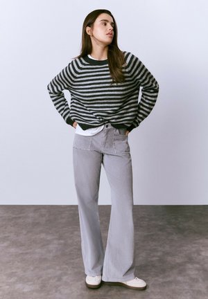 Suéter a rayas en gris y negro con un corte holgado, combinado con pantalones de piel de corduroy grises de pierna acampanada que presentan bolsillos decorativos y zapatillas blancas.