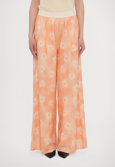 Pantalons larges en tissu orange avec un motif floral subtil. Dotés d'une taille élastique et d'une texture douce. Associés à des chaussures noires.