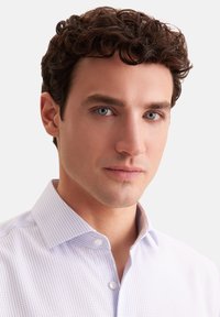 Witte overhemdd met een fijn blauw ruitpatroon, met een gebuttonde kraag en een gladde stof, gedragen door een persoon met kort krullend haar.