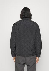 Schwarze gesteppte Jacke mit einem Rautenmuster, ausgestattet mit einem Stehkragen, langen Ärmeln und Seitentaschen. Glatte Textur und leichtes Design.