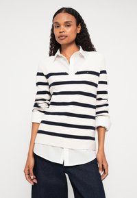 Gestreifter Pullover in Marineblau und Weiß mit V-Ausschnitt, langen Ärmeln und strukturiertem Strick. Über einem weißen Hemd mit Kragen getragen.