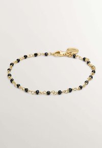 Pulsera de oro con cuentas facetadas negras, unidas por alambre retorcido. Incluye un cierre de langosta y un charm en forma de etiqueta circular.