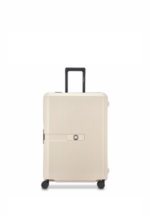 Maleta rígida beige con estrías verticales, asa negra retráctil, cerradura incorporada y cuatro ruedas giratorias negras sobre fondo blanco.