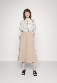Culottes bege claro com cintura elástica e bolsos laterais, combinados com uma blusa de mangas bufantes listrada em creme. Mules abertas pretas.