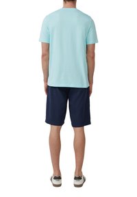 Lichtblauwe katoenen T-shirt met korte mouwen, gecombineerd met marineblauwe shorts. De persoon draagt witte sneakers met zwarte accenten.