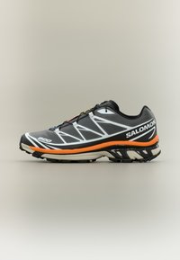 Μαύρο αθλητικό παπούτσι με λευκές λεπτομέρειες και πορτοκαλί μεσόσολα. Διαθέτει υφασμένο επάνω μέρος και ενισχυμένη εξωτερική σόλα από καουτσούκ για πρόσφυση.