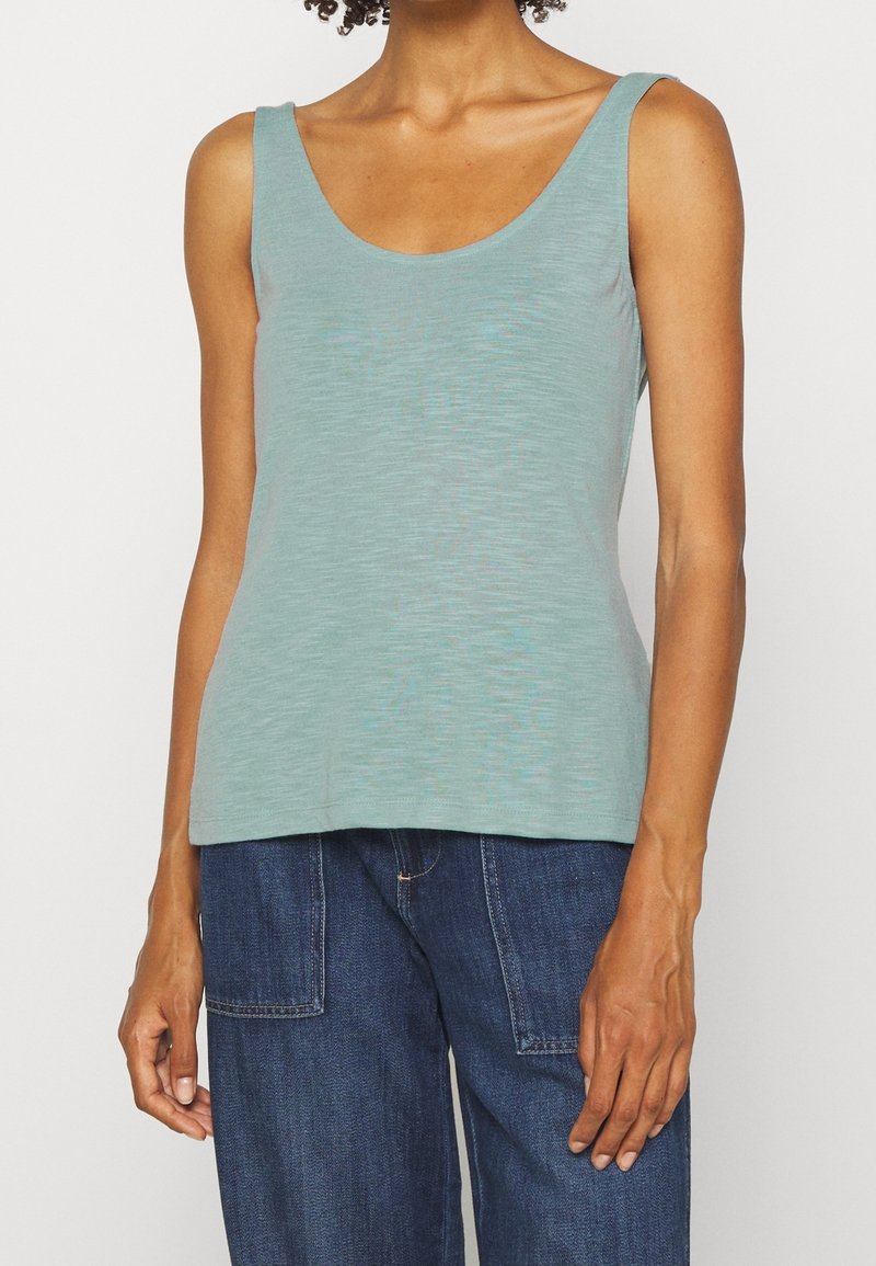 Ljus teal färgad linne gjord av mjukt tyg, med en rundad halsringning och tunna axelremmar. Slät textur utan ytterligare mönster.