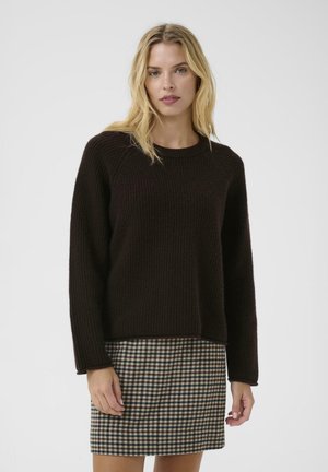 Brown ribbed sweater with a round neckline and long sleeves, paired with a plaid skirt in beige, black, and brown tones.