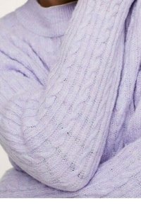 Close-up of a person wearing a light purple cable-knit sweater, showing detailed knit patterns on the sleeve and chest.