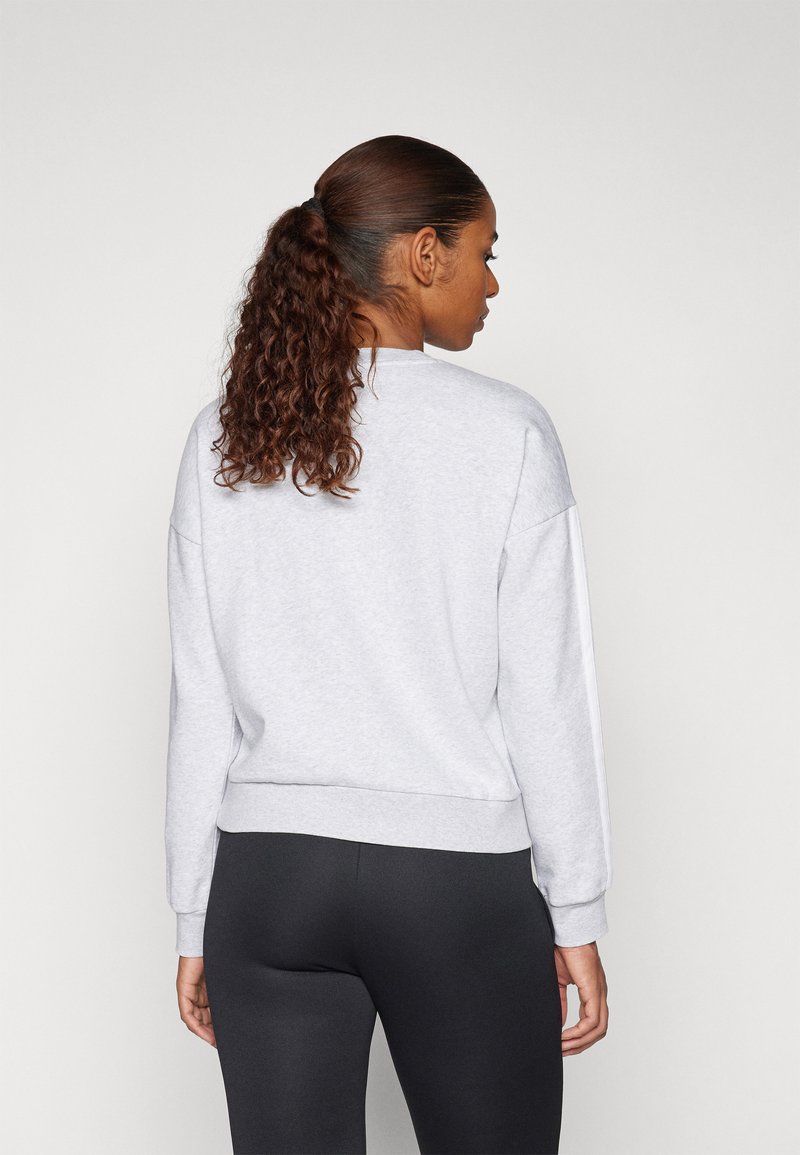 Világosszürke pulóver hosszú ujjakkal, bordázott mandzsettákkal és szegéllyel; pamut keverék anyag; fekete leggings-szel párosítva; hátulról látható.
