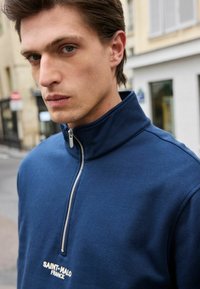 Felpa zip-up blu navy con colletto alto, dotata di una cerniera metallica centrale e con la scritta "SAINT-MALO FRANCE" ricamata in bianco.