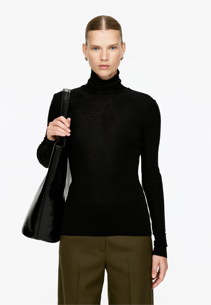 Black turtleneck sweater with long sleeves, made of a soft, thin material. Paired with olive green trousers and a large black leather bag.