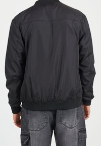 Černá bomber bunda s hladkou, lesklou texturou, pružnými manžetami a pasem, s jednoduchým designem bez dalších vzorů nebo ozdob.