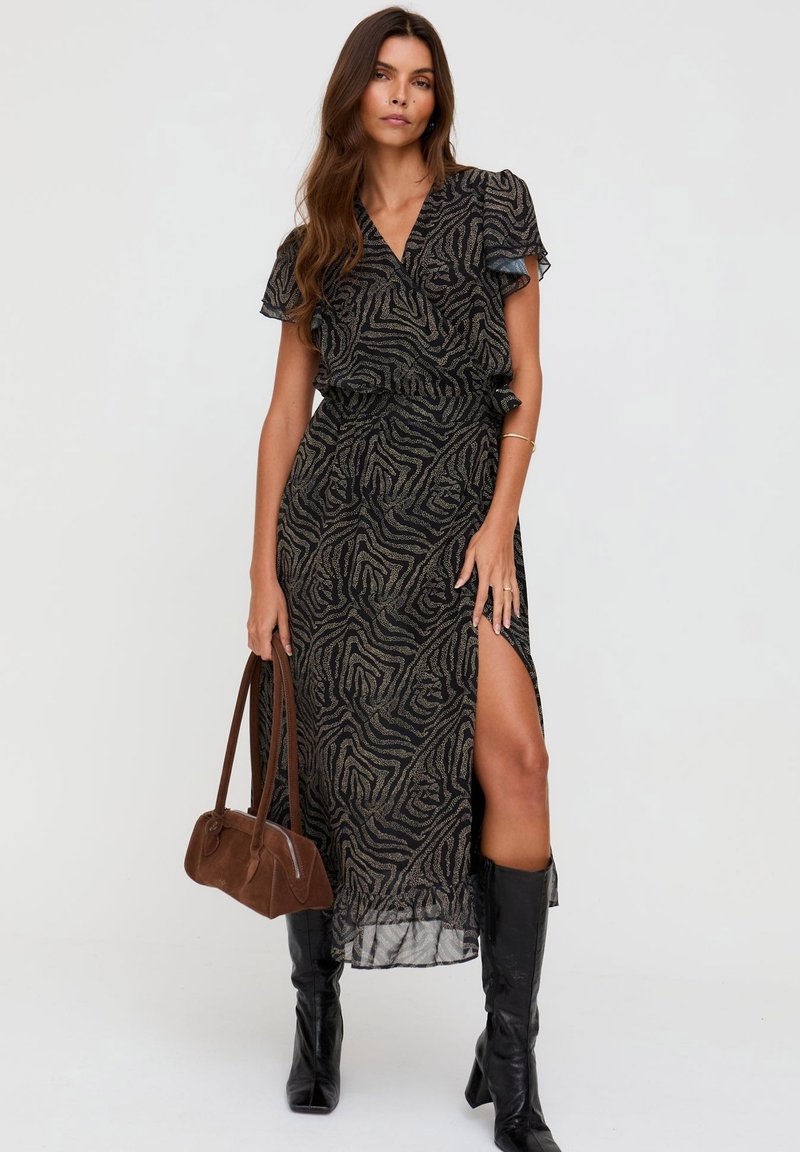 Schwarzes Maxikleid mit kurzen, gerafften Ärmeln, goldenem abstraktem Muster, seitlichem Schlitz, tailliert, kombiniert mit einer braunen Handtasche und kniehohen schwarzen Stiefeln.