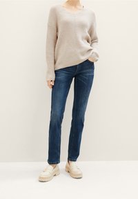 Beige ribbad stickad tröja med V-hals och diagonalt mönster, matchad med mörkblå raka jeans och krämfärgade plattformsmokasiner.