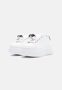 Białe trampki z grubą, żeberkowaną podeszwą, ozdobione czarnymi i kremowymi akcentami na sznurowadłach. Górna część z gładkiej skóry i okrągły nosek.