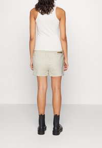 Shorts beige con dobladillo deshilachado, dos bolsillos en la parte posterior y una etiqueta marrón en la cinturilla. Un par de botas negras hasta el tobillo con una suela gruesa visibles.