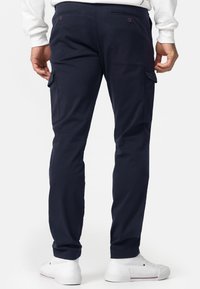 Pantalones cargo azul marino con bolsillos laterales, diseño ajustado, material de algodón y cierre con doble botón en la parte trasera, combinados con zapatillas blancas.