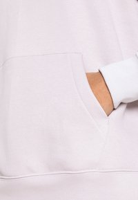 Ljus lavendel hoodie med en stor framficka, en mjuk textur och kontrasterande vita cuffs. Den har en enkel, avslappnad design.