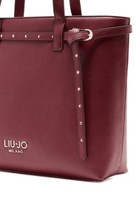 Bolso tote de cuero burdeos con superficie texturizada, detalles de herrajes plateados y logo en relieve. Presenta una forma estructurada y asas dobles.