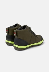 Zapatillas altas de lona verde con una suela de goma negra y acentos en verde brillante. Presentan un forro gris y ojales negros para los cordones.