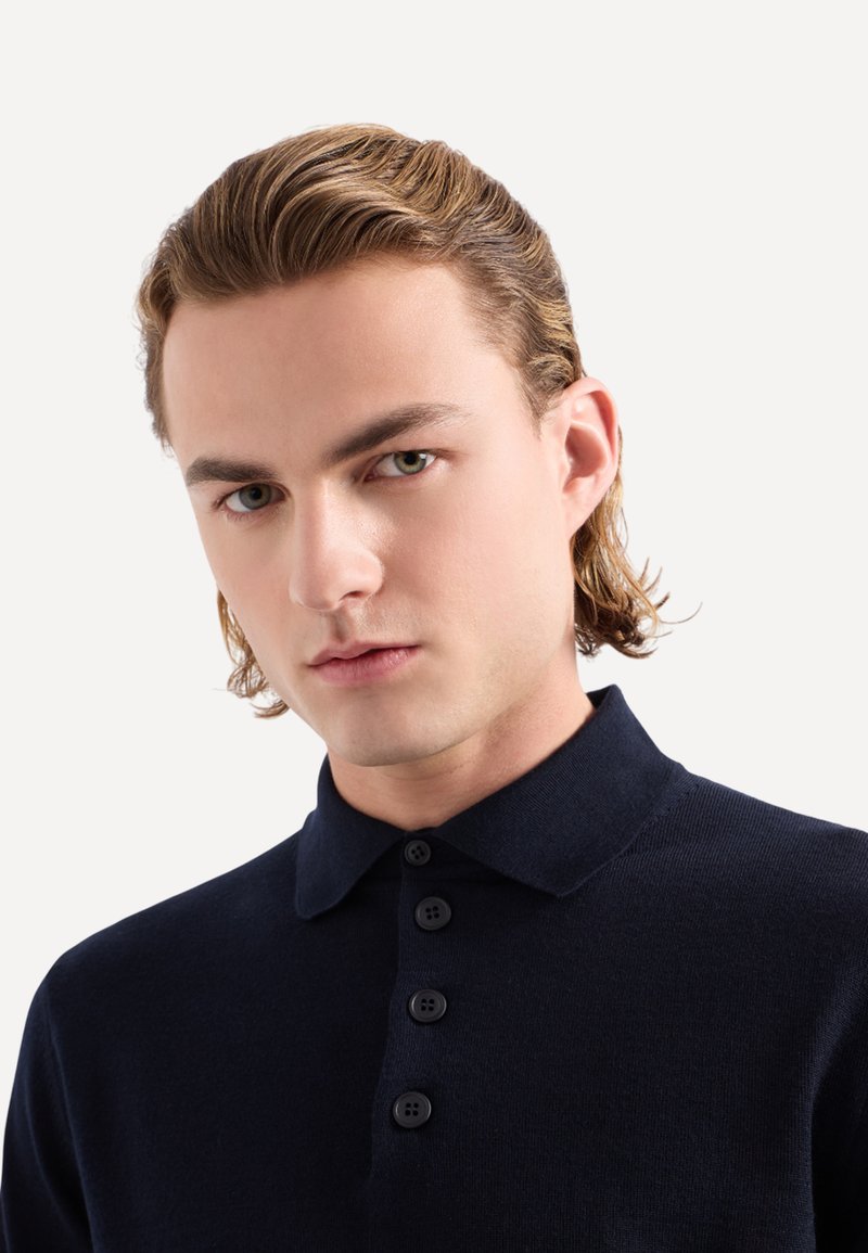 Polo shirt blu navy con maniche corte, realizzato in un materiale a maglia morbido. Presenta un colletto classico e quattro bottoni neri sulla parte anteriore.