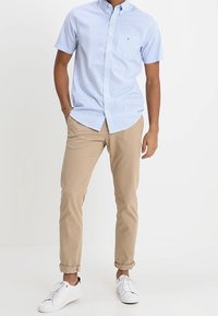 Camicia a maniche corte a scacchi blu e bianchi, chinos color khaki e sneaker bianche. La camicia presenta un colletto button-down e un dettaglio base della tasca.