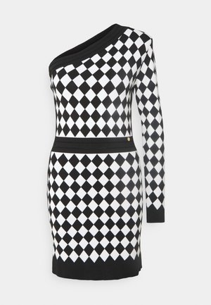 Robe asymétrique noire et blanche à motif losange, silhouette ajustée et manches longues. Ceinture noire contrastante.