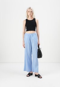 Zwarte mouwloze crop top, lichtblauwe gestreepte wijde broek, zwarte open-toe blokhakken sandalen en een kleine zwarte handtas.