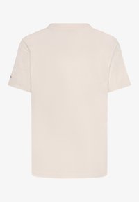 Camiseta de manga corta color crema con cuello redondo, hecha de algodón. Presenta un diseño liso y un pequeño acento en la manga izquierda.