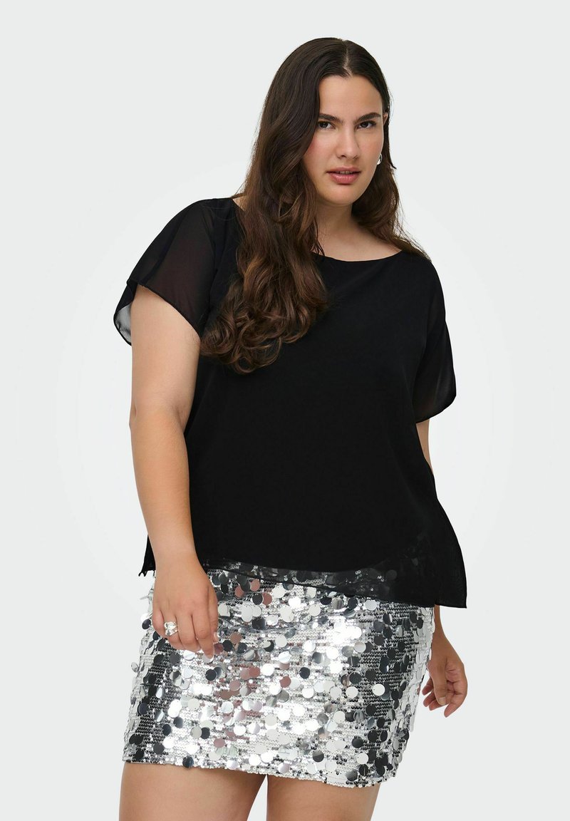 Sort bluse med korte ærmer og løs pasform, parret med en sølvfarvet miniskirt dækket af cirkulære pailletter, der reflekterer lyset.