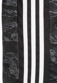 Czarna i szara tkanina o teksturowanym wzorze z trzema wyraźnymi białymi paskami biegnącymi pionowo. Materiał wydaje się miękki i elastyczny.