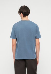 T-shirt à manches courtes en tissu bleu délavé, avec un col rond et un ourlet droit. Texture lisse avec des détails de couture minimes.