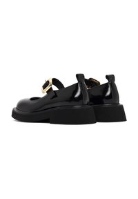 Schwarze Lacklederschuhe mit runder Zehenpartie, verstellbarem Riemen und goldener Schnallenverzierung. Klobiger schwarzer Absatz mit einer strukturierten Oberfläche.
