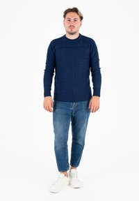 Sweter w morski wzór z teksturowanym deseniem, okrągłym dekoltem i długimi rękawami, w połączeniu z jasnoniebieskimi dżinsami i białymi trampkami.