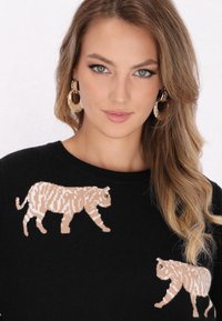 Pullover nero con due motivi di tigre beige sul davanti, lavorato a maglia in modo intricato. Il collo è rotondo e la texture è liscia.