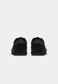 Sapatos de desporto pretos com uma textura suave, design discreto e detalhes subtis no calcanhar. Sola de borracha flexível com padrão de aderência.