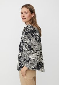 Blusa a maniche corte con un motivo astratto in bianco e nero, realizzata in tessuto leggero, con una vestibilità comoda e colletto classico.