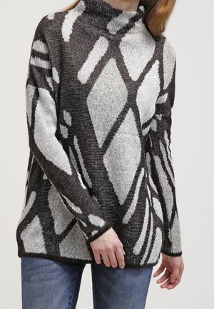 Knit sweater featuring a high neck, black and white geometric patterns, loose fit, and textured fabric. Worn with denim jeans.