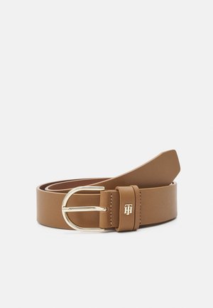 Brown leather belt with gold oval buckle and small engraved metal logo detail on belt loop, coiled on white background.